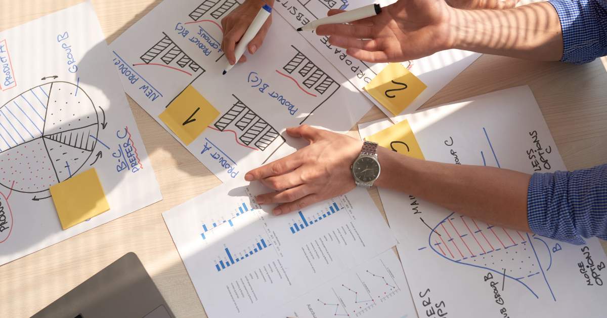 Das Bild zeigt die H&auml;nde zweier Personen und jede Menge Unterlagen mit Graphen und Diagrammen