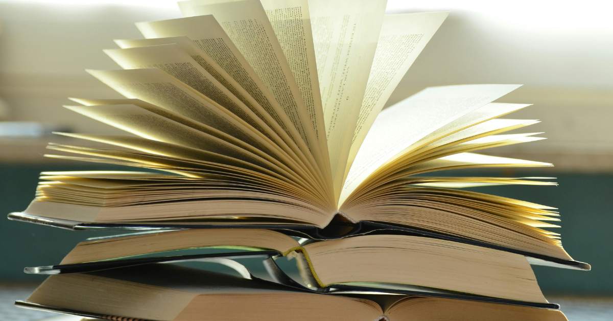 Das Bild zeigt einen Stapel B&uuml;cher. Das oberste Buch ist aufgeschlagen. Der Hintergrund ist verschwommen