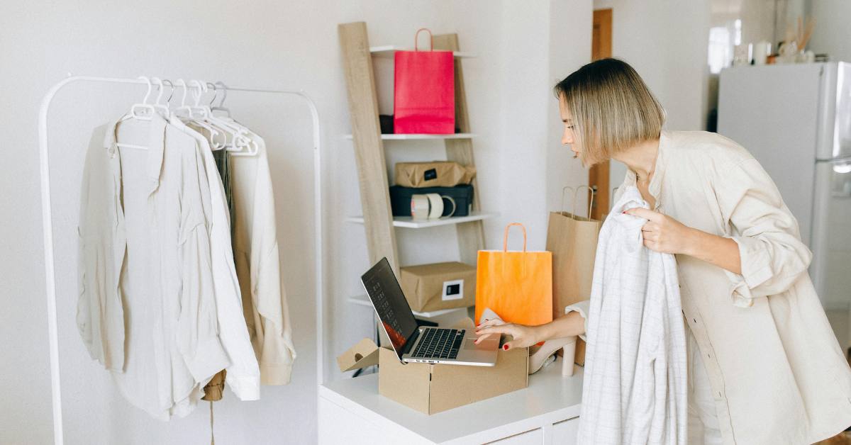 Frau mit Kleidung und T&uuml;ten drumherum, beim Online-Shopping am Laptop