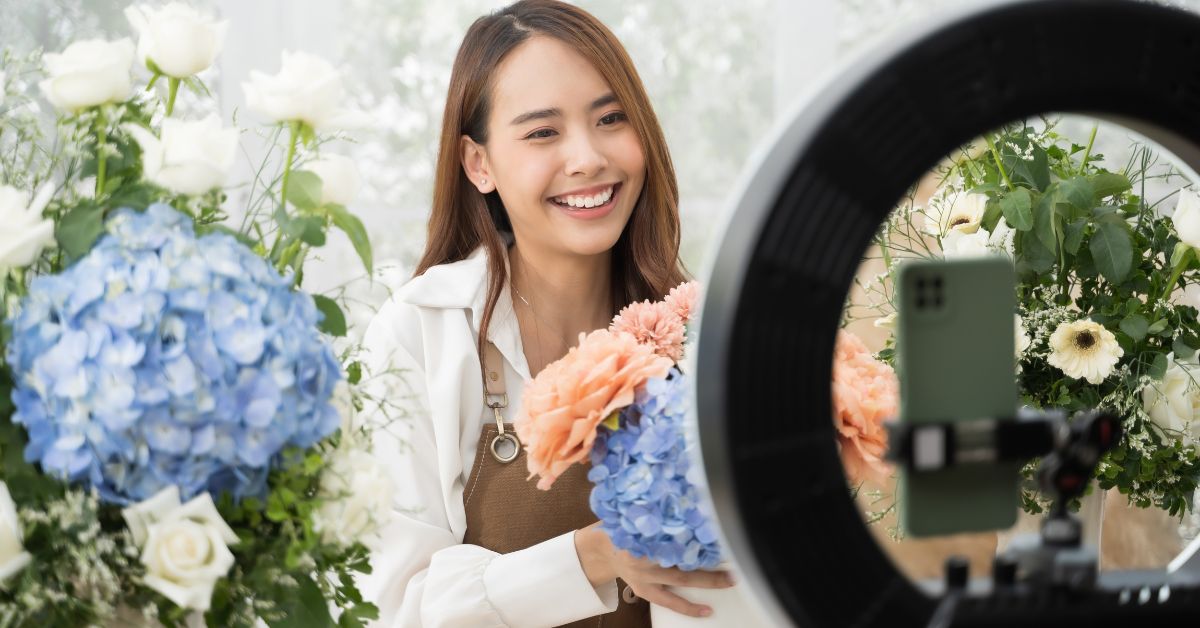 Eine Frau pr&auml;sentiert Blumen vor einem Ringlicht und einem Smartphone